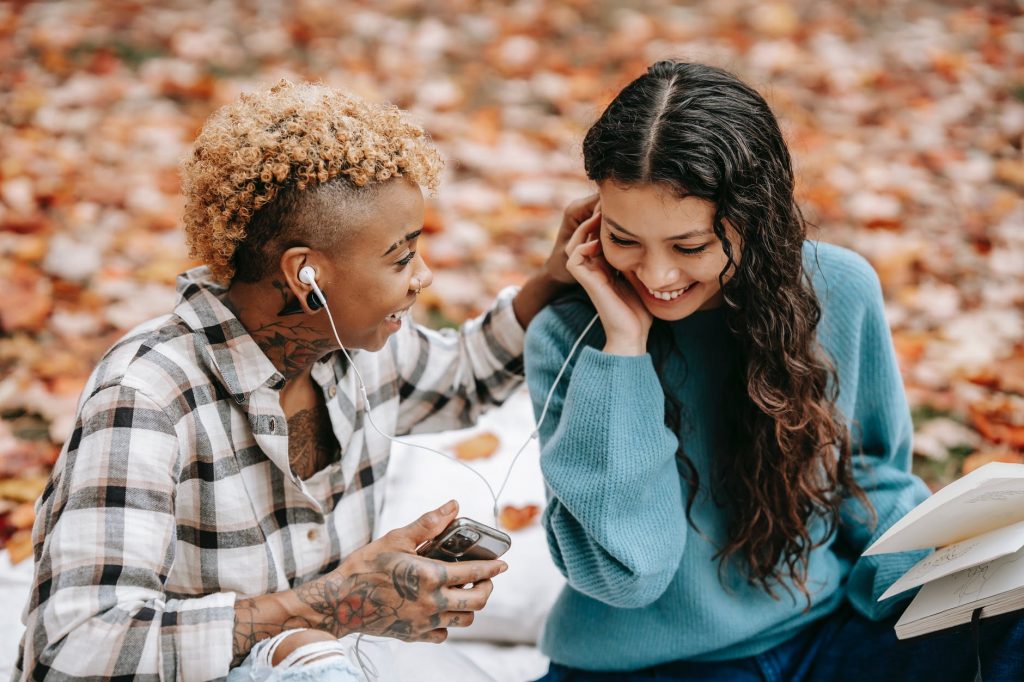 happy multiethnic friends listening to music in earphones in park