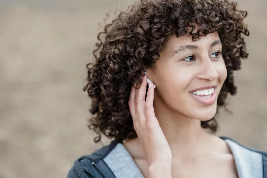 happy ethnic woman listening to music in wireless earbuds